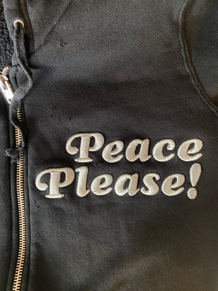 CLOSE UP IMAGE OF PEACE PLEASE! EMBROIDERY AND DISTRESSED DETAILS ON FABRIC.