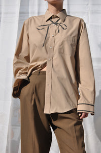 MODEL WEARING TAN REPURPOSED BUTTON DOWN SHIRT WITH HAND PAINTED BOW TIE AND CONTRAST BINDING AT CUFFS.