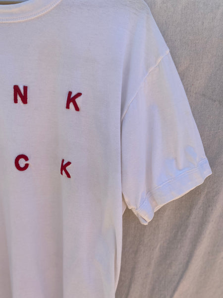 CLOSE UP VIEW OF LEFT SLEEVE AND NK CK EMBROIDERY IN RED.
