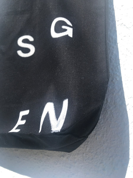 ZOOMED IN VIEW OF BOTTOM CORNER OF TOTE BAG. PRINTED LETTERS S G E N IN WHITE ALSO VISIBLE.