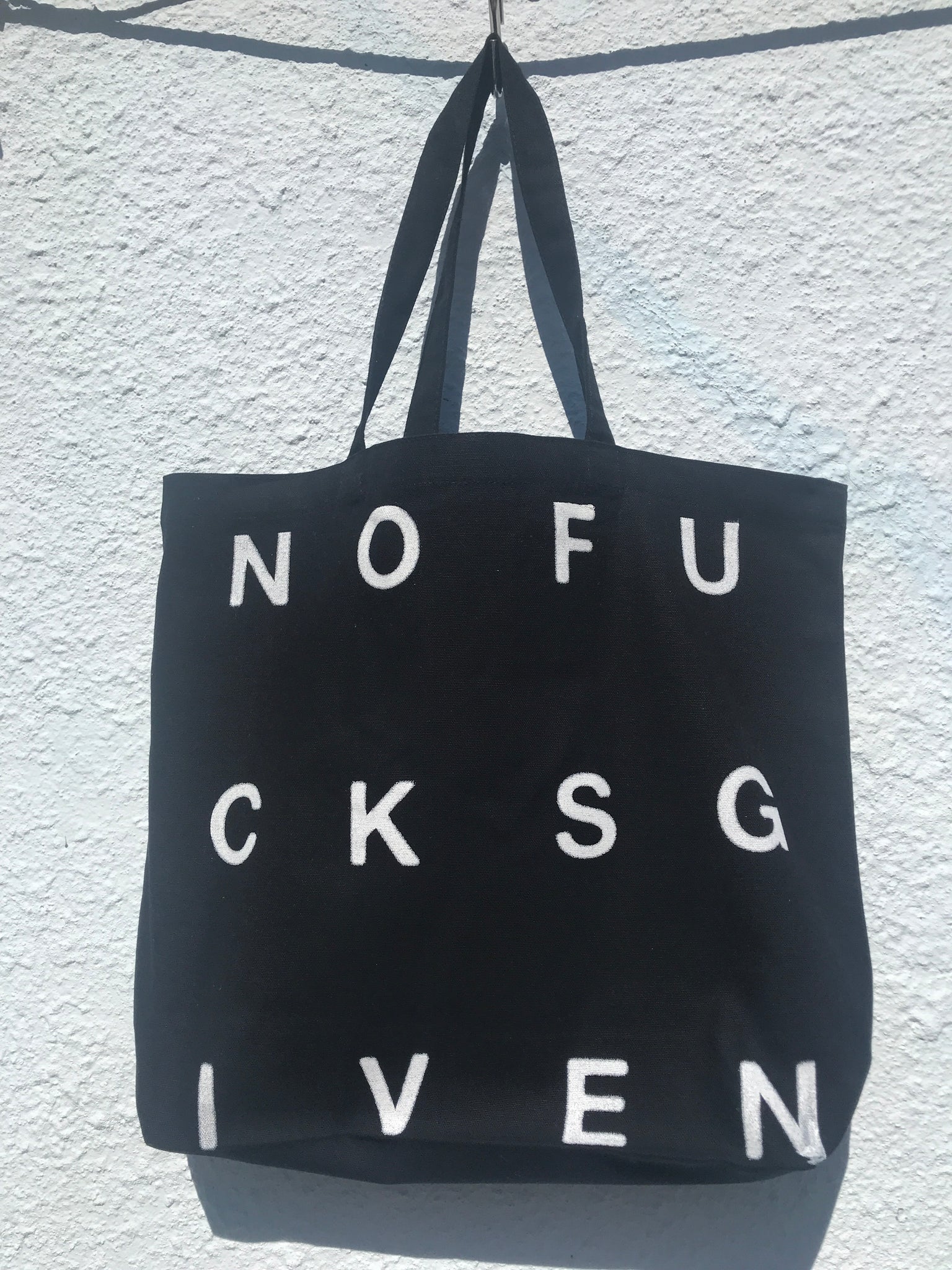 FRONT VIEW OF BLACK TOTE BAG WITH NOFUCKSGIVEN PRINT IN WHITE.